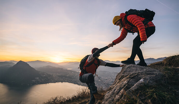 woman-helping-man-climbing-top-of-mountain-hiking-bdo