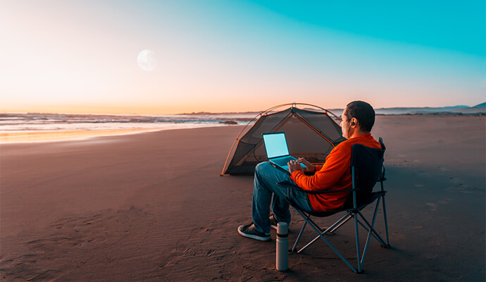 man-camping-on-beach-working-on-laptop-bdo