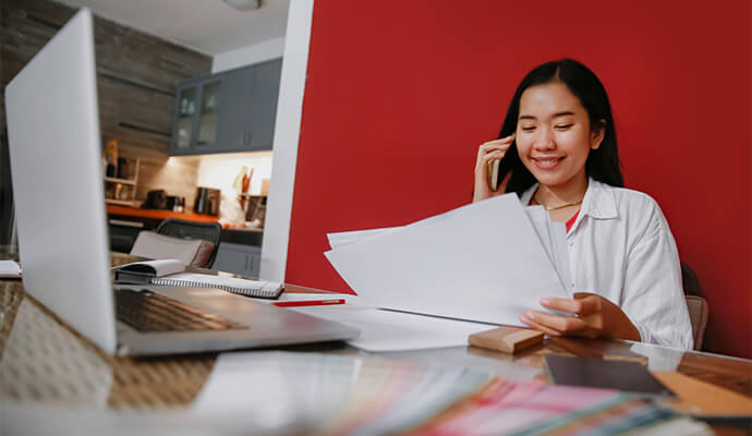 woman-smiling-on-the-phone-looking-at-documents-working-on-computer-bdo