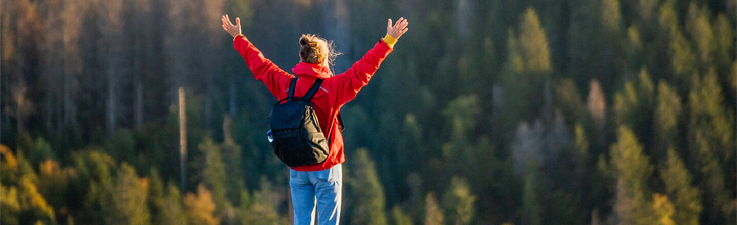 woman-with-arms-in-the-air-at-top-of-mountain-forest-landscape